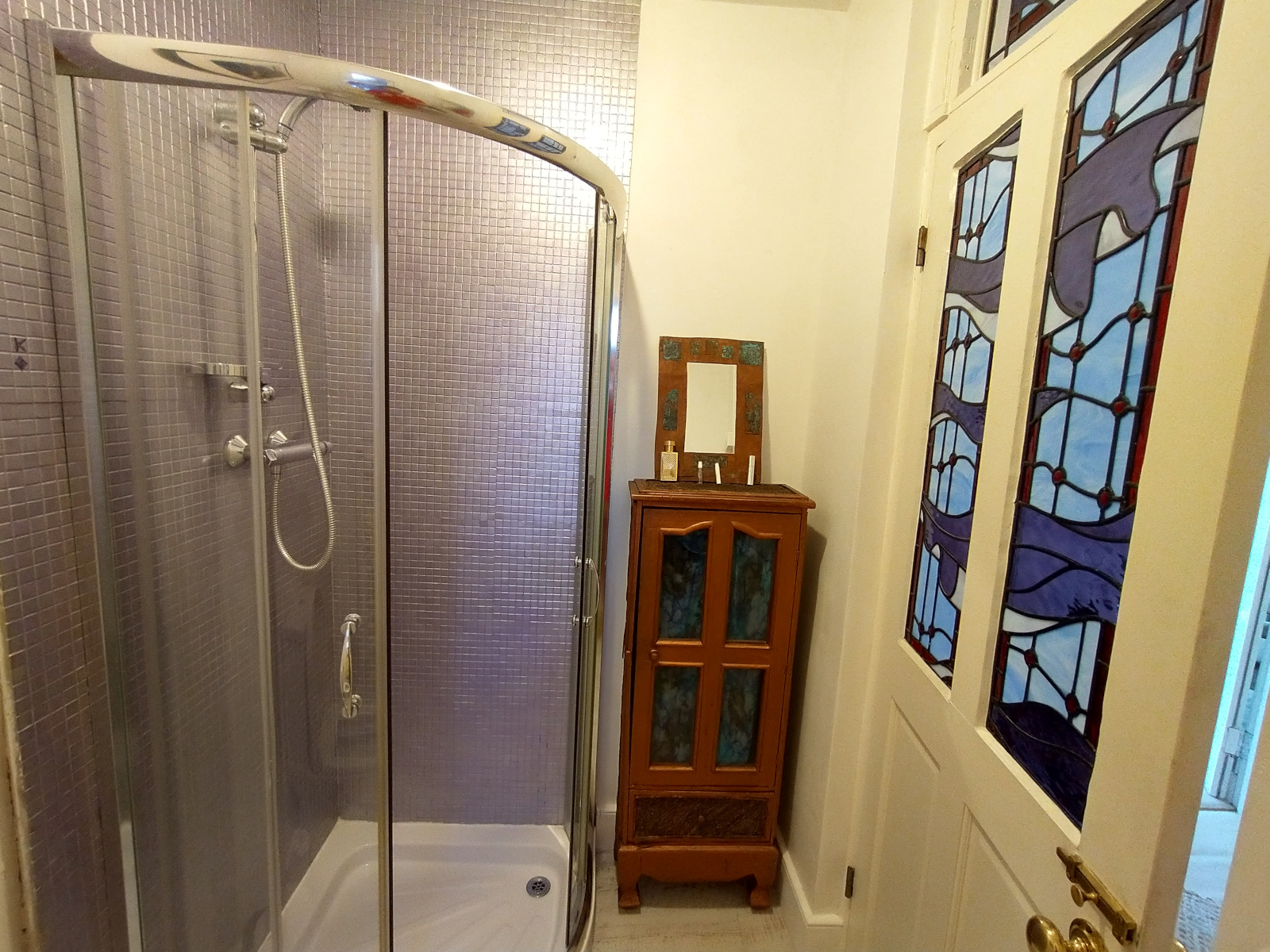 Bathroom with large shower cubicle, interestingly decorated with stained glass in the door